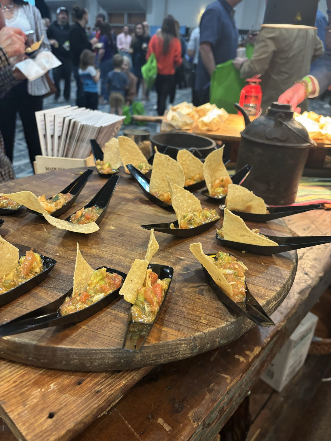 Wooden cutting board featuring serving boat spoons, each with a tortilla chip and salsa.