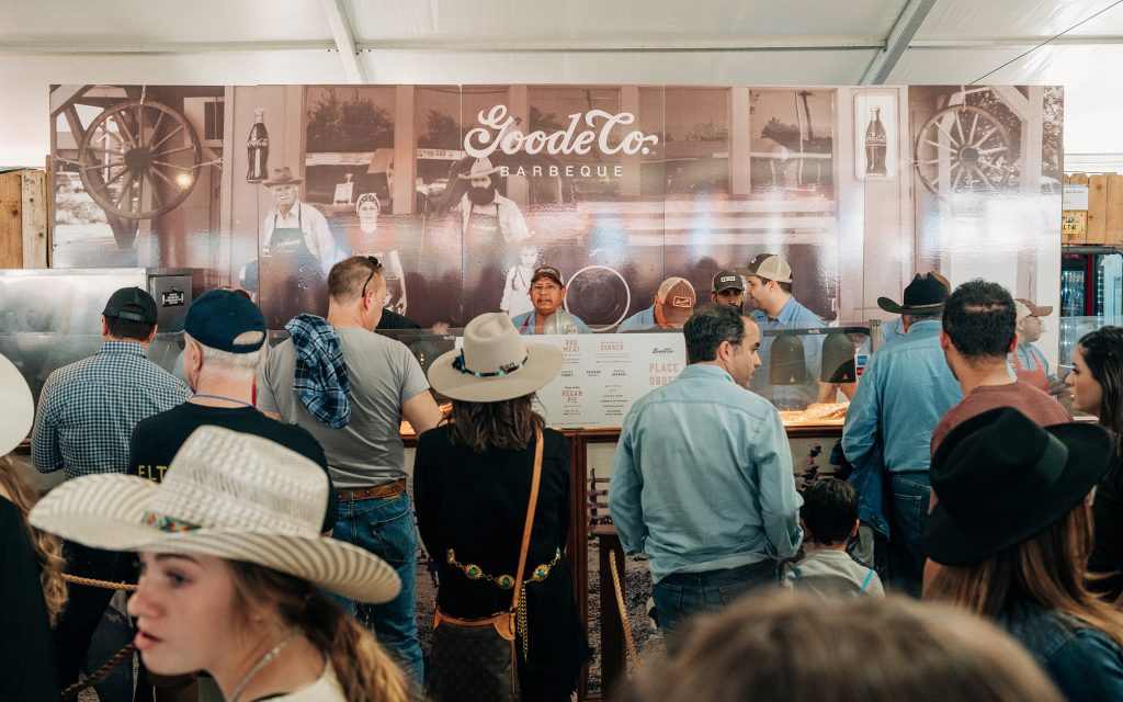 Photo of Goode Co. BBQ concession with rodeo patrons lined up and employees serving them in the background.