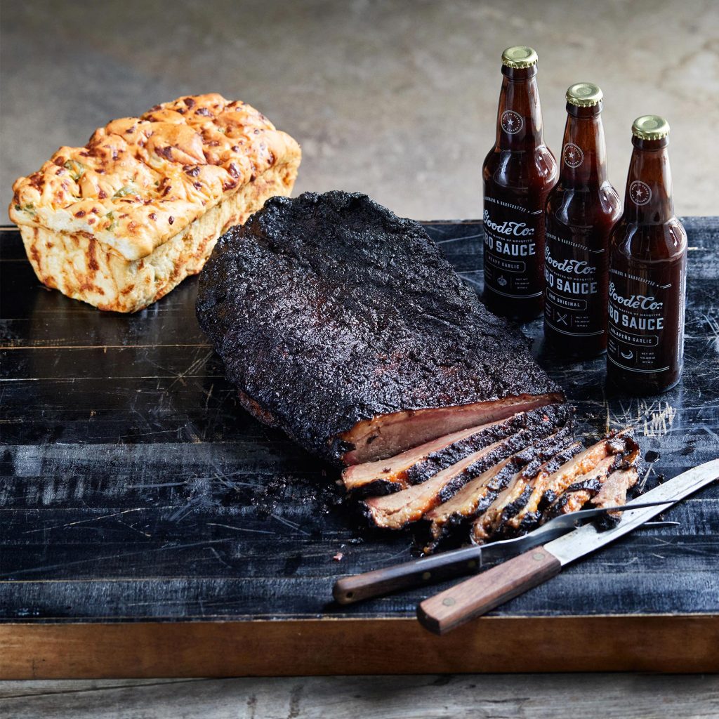 Sliced brisket on a wooden cutting board, with a whole loaf of jalapeno cheese bread to the side.