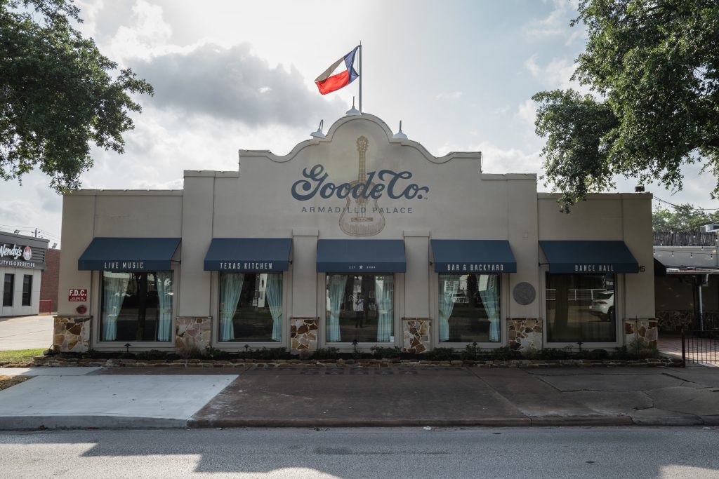 Exterior photo of the Armadillo Palace restaurant with the Texas flag flying high and the Goode Co. logo on the front.