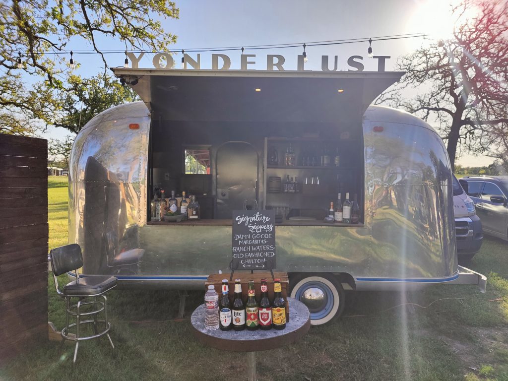  Picture of open doors on the Yonderlust with a full bar in the airstream in the background and a table of beers in the front. 