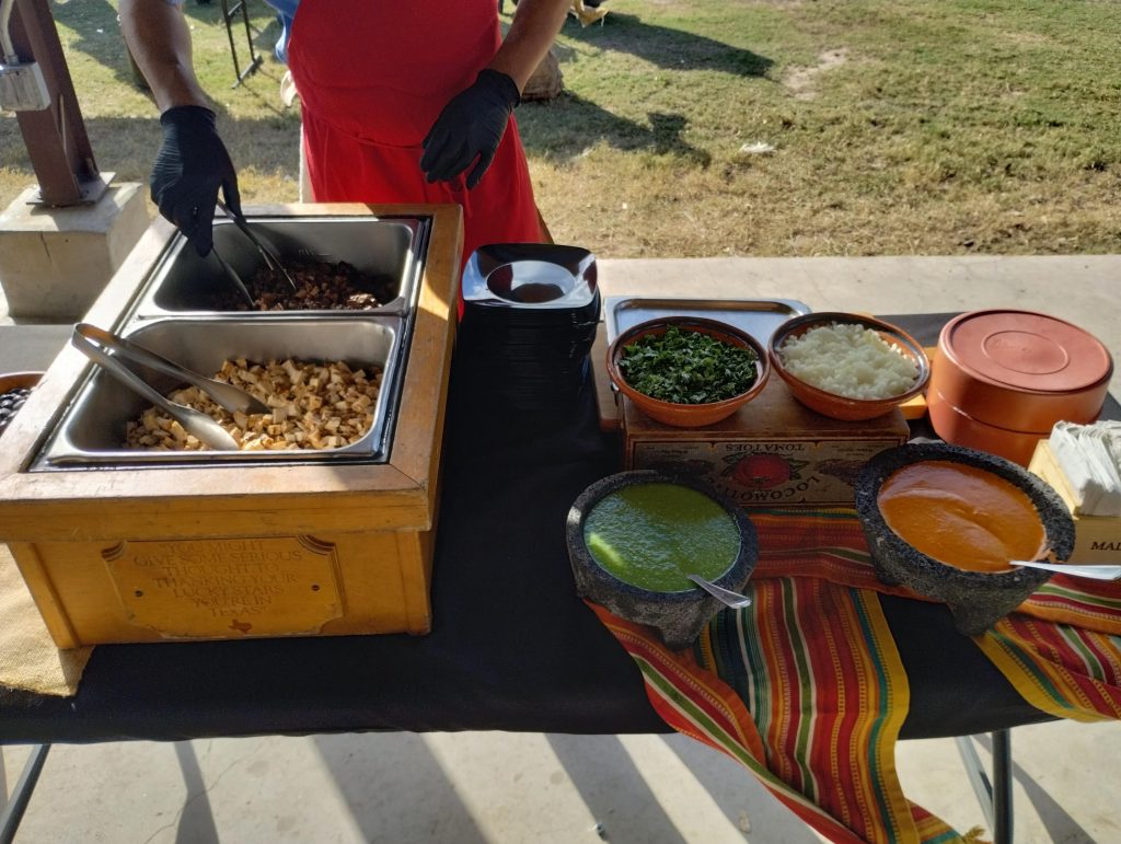 A taco stand at a catered event featuring diced chicken and beef, as well as cilantro, red and green salsa, onions, and tortillas.