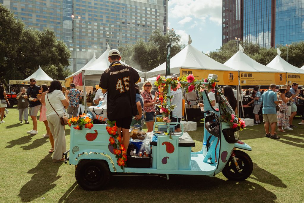 A football fan in a small turquoise cart serving drinks and finger foods outdoors.